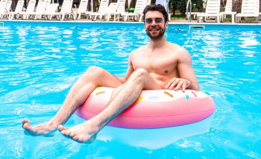 Gülümseyen sakallı adam şişme yüzük kullanırken havuzda eğleniyor. Güneş gözlüklü adam. Yaz zamanı, tatiller, yaşam tarzı konsepti