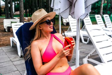 Güzel genç bayan güneşlenirken yüzme havuzunun yanında dinleniyor. Mutluluk duygusu, yaz tatili konsepti.