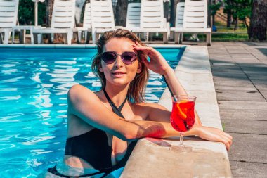 Güneş gözlüklü gülümseyen kadın hafta sonunu açık havuzda geçirir ve kokteylden zevk alır. Uzayı kopyala Yaz, tatil ve yaşam tarzı konsepti