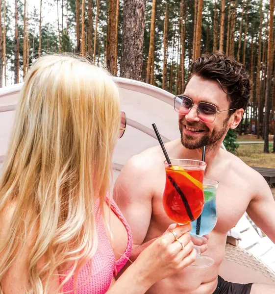 stock image Smiling young man looking at his girlfriend while toasting cocktails, enjoying the rest near pool. Summer vacation, relationship, lifestyle concept