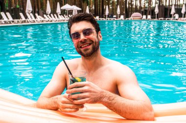 Yüzme havuzunda dikilmiş, hafta sonunun tadını çıkaran mutlu sakallı bir adam. Yaz zamanı, tatiller, yaşam tarzı konsepti