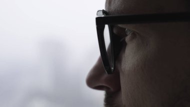 Gözlüklü, dikilip pencereye bakan, odaklanmış beyaz bir erkek. Yaşam tarzı konsepti. Ağır çekim. Kapatın. Boşluğu kopyala