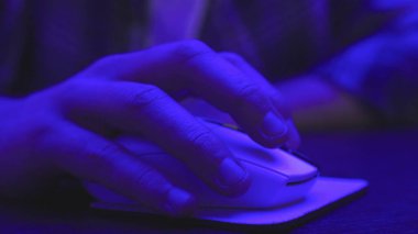 Karanlıkta bilgisayar faresi kullanırken masada oturan genç adam. Kapatın. Çevrimiçi çalışma, iş ve teknoloji konsepti. Yavaş çekim