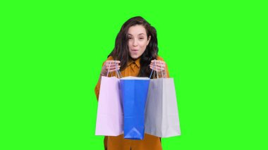 Ayakta duran ve yeşil izole edilmiş arka plandaki alışveriş paketlerine bakan mutlu beyaz kadın. Kara Cuma, satış konsepti
