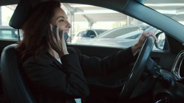 Elinde akıllı telefon olan gülümseyen kadın, park yerinde araba süren ve internetten arayan. Yavaş çekim videosu