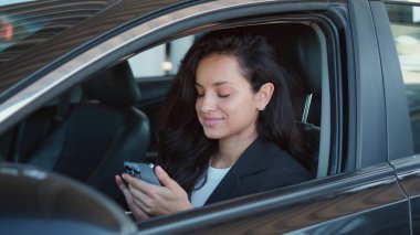 Açık camlı arabada oturan, rahatlayan, akıllı telefonda yazan bir kadın portresi. Yavaş çekim videosu