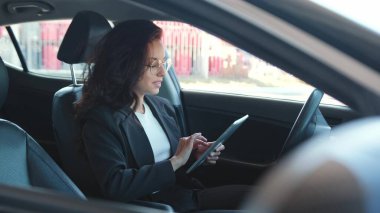 Mutlu kadın portresi açık camlı arabada oturuyor, rahatlıyor, tablet üzerinde yazıyor. Yavaş çekim videosu