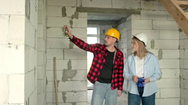 Elinde mezurası olan bir inşaatçı ve bitmemiş evdeki duvarlara bakan bir yönetici. Yavaş çekim