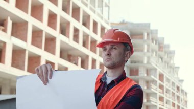 Tamamlanmamış çok katlı evin önünde dururken müteahhit danışmanlık çizimlerinin portresi. Yavaş çekim