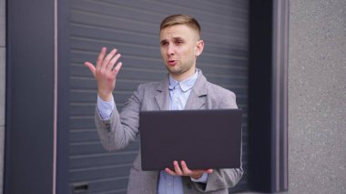 Genç adam dışarıda duruyor, dizüstü bilgisayarla çalışıyor, el hareketlerini gösteriyor. İş, iş, teknoloji konsepti. Yavaş çekim