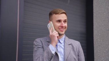 Açık havada kahvenin tadını çıkarırken akıllı telefondan konuşan genç ve mutlu bir iş adamı. İş, iş, teknoloji konsepti. Yavaş çekim