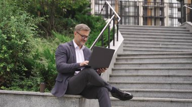 Gözlüklü bir iş adamı dışarıda çalışırken dizüstü bilgisayar kullanıyor. İş, iş, teknoloji konsepti. Yavaş çekim