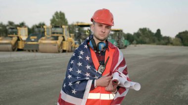 Koruyucu miğferli ustabaşı ve üzerinde taslak olan giysiler. Amerikan bayrağıyla kaplanmış bir adam. Yavaş çekim fotoğrafı