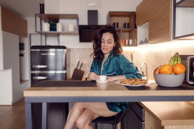 Sakin, esmer, seksi, ipek bornozlu bir bayan. Evdeki barda oturmuş kahvesinin tadını çıkarıyor. Sabah rutini, ev hayatı