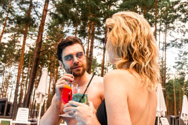 Güneş gözlüklü yakışıklı genç bir adam ve dışarıda birlikte otururken ferahlatıcı içecekler içen sarışın bir kadın. Dinlenme ve rahatlama kavramı