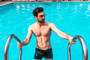 Güneş gözlüklü şık bir adam güneşli bir günde yüzmeye giderken dinleniyor. Uzayı kopyala Yaz zamanı, tatiller, yaşam tarzı konsepti