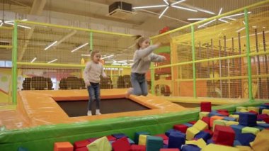 Trambolinde oyun parkında oynayan mutlu küçük kızlar. Yumuşak köpük renkli küplerle. Ağır çekim. Çocukluk, eğlence, eğlence parkı konsepti