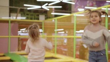 Büyük oyun parkında renkli trambolinde zıplamaktan zevk alan iki küçük kız, birlikte eğlenceli vakit geçiriyorlar. Ağır çekim. Çocukluk, eğlence, eğlence parkı konsepti