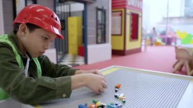 Oyun merkezinde oynarken renkli plastik tuğlaları olan güvenli kask takan Afrikalı Amerikalı küçük çocuk. Ağır çekim. Çocukluk, eğlence, meslek kavramı