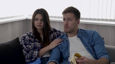 Karantina sırasında genç bir çift oturma odasında. Birlikte oturup film izleyelim, muz yiyen adam. Plastik, kağıt ve cam çöplerle çevrili bir çift. Kamera geri gidiyor