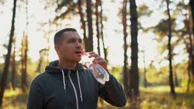 Ormanda ya da parkta koşudan sonra plastik atık şişesinden su içen bir adam. Tam HD görüntüler