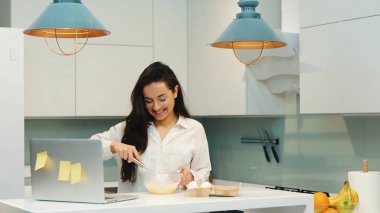 Karantina sırasında evde çalışan genç bir kadın. Kız görüntülü konuşuyor ya da arıyor ve gülümsüyor. Yumurtaları bown 'da karıştırıp kahvaltı hazırlamak. Çoklu görevdeki kişi