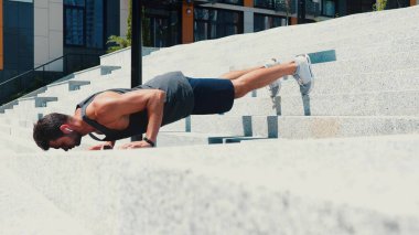 Genç adam dışarıda egzersiz yapıyor. Sportif adam caddedeki basamaklarda şınav çekiyor. Fitness aktivitesi, egzersiz ya da tek başına antrenman. Kulaklıkla müzik dinle.