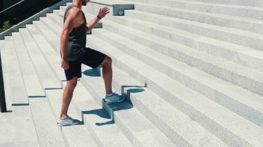 Genç adam dışarıda egzersiz yapıyor. Hareketsiz duran güçlü adam bir adım atlıyor. Beyaz kulaklıkla müzik dinle. Dışarıda tek başına çalışmanın tadını çıkar. Güneşli güzel bir gün