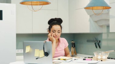 Karantina sırasında evde çalışan genç bir kadın. Yorgun kız kulaklık takıyor ve neşeyle konuşmaya başlıyor ve gülümsüyor. Evden internet üzerinden çalışıyor. Yemek pişirdikten sonra günün sonunda