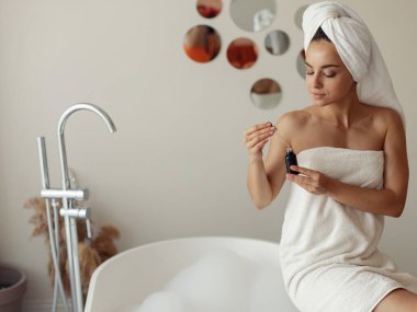 Genç ve güzel bir kadın sabah güzellik ayinlerinde kozmetik kullanıyor. Modern banyodaki evinde elinde bir şişe serum tutan beyaz bir kadın. Cilt bakımı, yüz bakımı