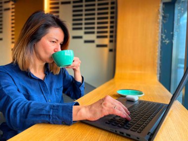 Kafkasyalı bir kadın kafede kahve içerken internette dizüstü bilgisayarda geziniyor. Kafeteryada kahve molası sırasında bilgisayardaki kadın profesyonel daktiloya yakından bak. Monitöre bak.