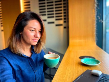 Kafede oturup internetten dizüstü bilgisayara bakan mutlu, güzel bir kadın. Kadın serbest çalışan bayan iş kadını laptopla çalışırken kahve içer. Çalışma konsepti