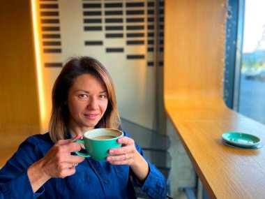 Kahvehanede otururken elinde kahve fincanı tutan ve kameraya bakan mutlu ve çekici bir kadın. Pencerenin yanındaki kafede kahve içen genç ve güzel bir bayan var. Boş zaman. Dinlenme kavramı