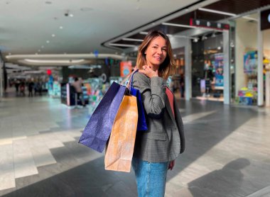 Oldukça çekici bir kadının portresi. Omzunda alışveriş merkezinde dururken kameraya bakıp gülümseyen bir sürü alışveriş çantası tutuyor. Sezonluk alışveriş. Alışverişkolik kavram