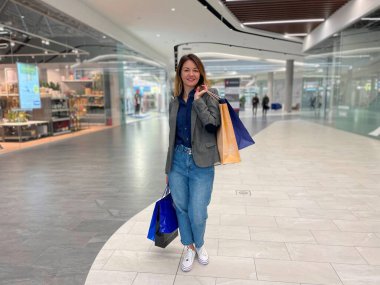 Alışveriş merkezinde durup alışveriş yaptıktan sonra kameraya bakıp gülümseyen orta yaşlı beyaz bir kadın. Mutlu yüz ifadesi olan güzel bir kadın kağıt torba tutuyor. Satın alma kavramı