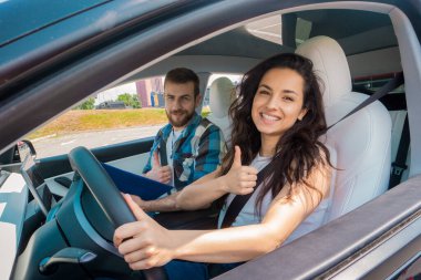 Gülümseyen genç bayan stilimli araba kullanıyor ve erkek eğitmen yolcu koltuğunda oturuyor. Test sürüşü, ulaşım, güvenlik, eğitim kavramı