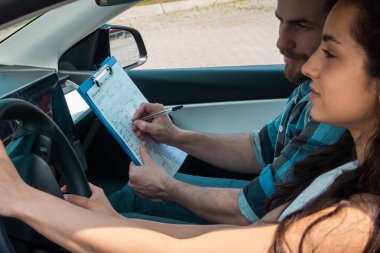 Sürüş testi raporunu tutan erkek eğitmen ve kız öğrenci araba kullanırken notlar alıyor. Test sürüşü, ulaşım, güvenlik, eğitim kavramı