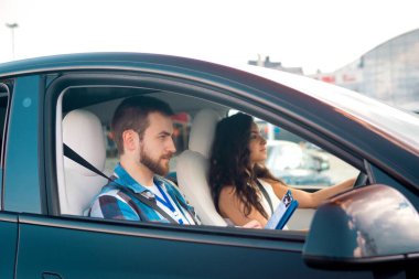 Genç bir erkek eğitmen, sürüş dersi sırasında araba kullanan bayan yola bakarken formda yazıyor. Ehliyet sınavı, ehliyet kursu, sınav konsepti.