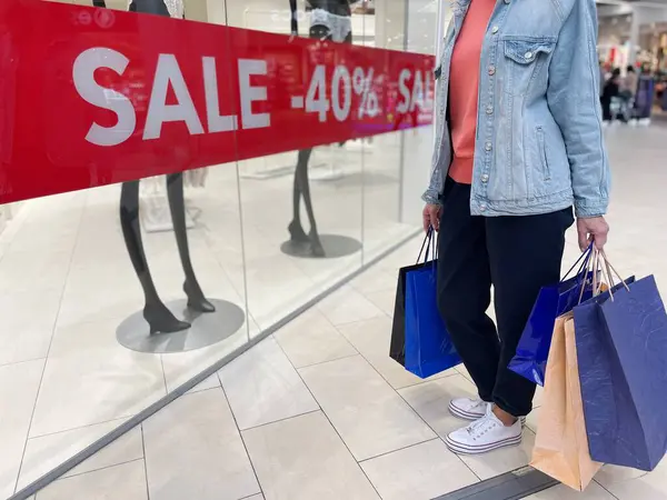 Mağaza vitrininin önünde elinde bir sürü alışveriş torbası tutan bir kadın. Alışveriş merkezindeki kadınların yakın çekimleri, ellerinde alışverişlerle. Sezon satışları. Alışverişkolik kavram