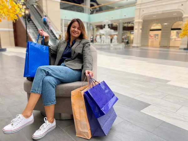 Alışveriş merkezinin içinde bol kesekâğıdı ve gülümseyen günlük kıyafetlerle oldukça neşeli bir bayan. Kafkasyalı mutlu kadın kameraya bakarak alışveriş torbaları dolusu para harcadı.