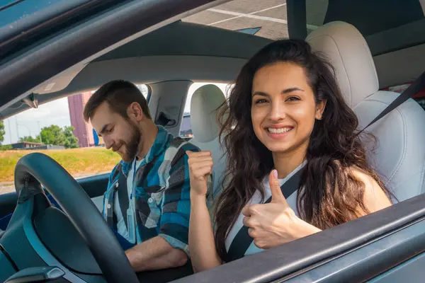Test sürüşü sırasında başparmağını gösteren mutlu güzel bir kadın. Gülümseyen erkek eğitmen bayanın yanında oturuyor. Test sürüşü, ulaşım, güvenlik, eğitim kavramı