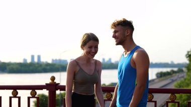 Happy young couple of athletes standing outdoors speaking and laughing together. Portrait of Caucasian man and woman talking after workout in street. Sporty lifestyle. Healthy activity. Communication