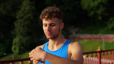 Close up of handsome young sportsman drinking water from bottle standing outdoor and looking away after exercising. Caucasian fit man in sportswear drink water on street on sunny day. Active lifestyle
