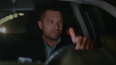 Takım elbiseli, yakışıklı, beyaz iş adamının gece araba sürüşünü ve etrafa gülümsemesini yakından takip edin. İş yerinden arabayla gelen bir adam. Taksi şoförü akşamları çalışıyor. Ağır çekim. Lüks stil