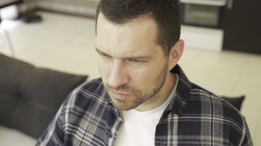 Gülümseyen sakallı adam evdeki kanepede oturmuş bardakları yerleştiriyor ve ileriye bakıyor. Yaşam tarzı konsepti. Yavaş çekim