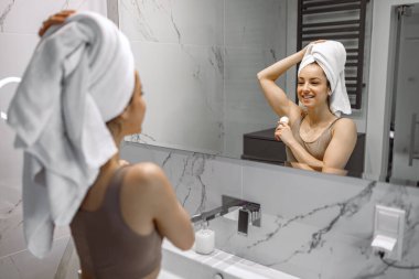 Beyaz havluyla mutlu bir kadın. Banyo deodorantına terleme önleyici koyuyor. Günlük hijyen prosedürleri, sağlıklı vücut bakımı kavramı