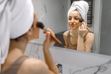 Yüzü kızaran bir fırçayla makyaj yaparken aynanın yanında duran güzel bir kadın. Güzellik ve Tedavi konsepti