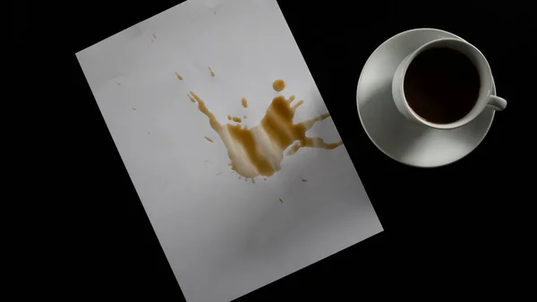 Paper with coffee spilled on it, drinking filter coffee on black table, white cup and coaster, isolated on black background, top view