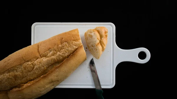 Cut bread into slices, bread slices on chopping board with knife, isolated on black background, top view