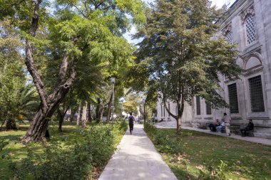 İnsanlarla dolu Sehzade Camii Bahçesi, yeşil çimenli ve ağaçlı düz taş yol, Ehzade Paa Camii dış görünüş, sehpa tarihi eserler: Fatih, İstanbul, Türkiye - 20 Eylül 2022 